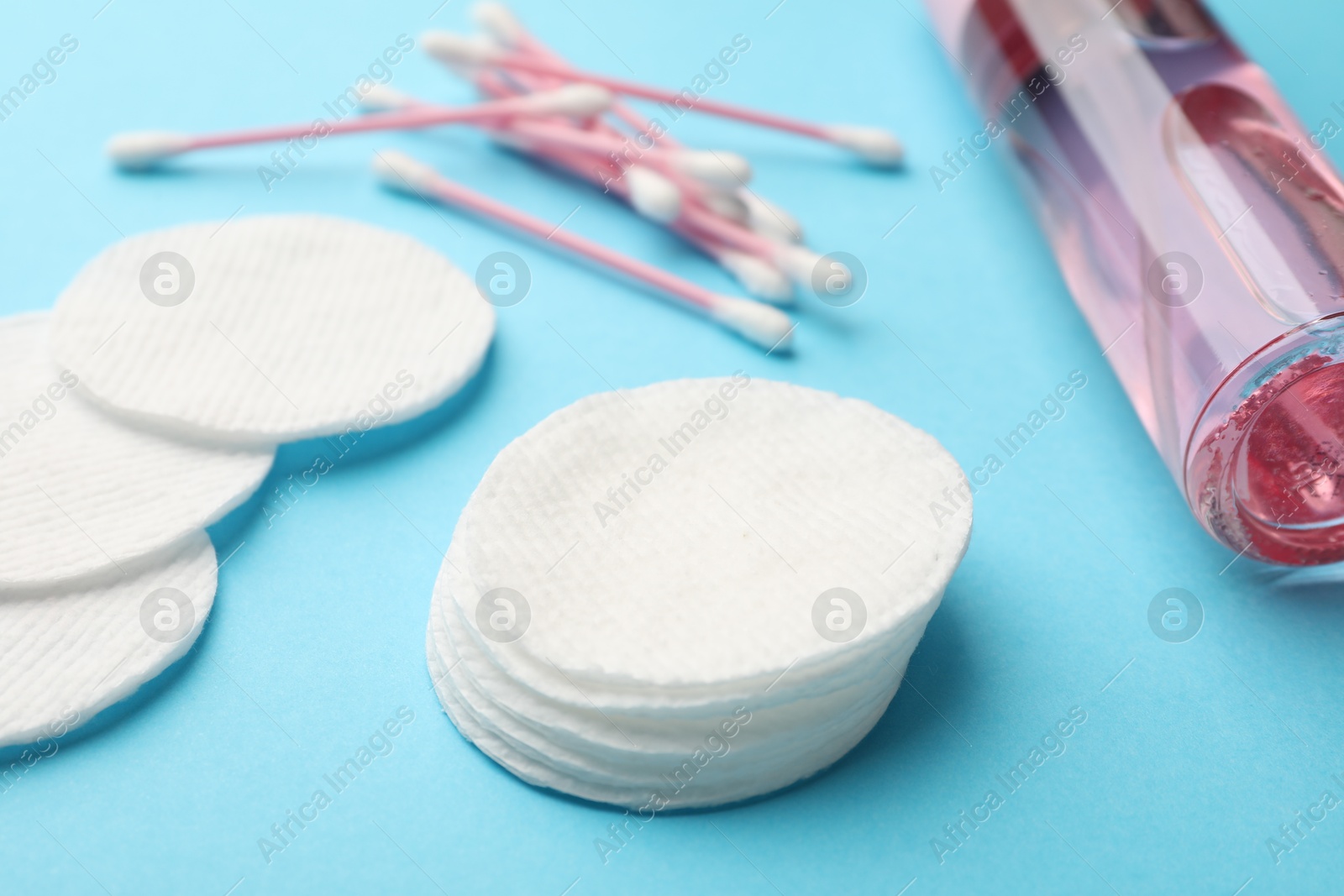 Photo of Cotton pads, bottle of cosmetic product and swabs on light blue background, closeup