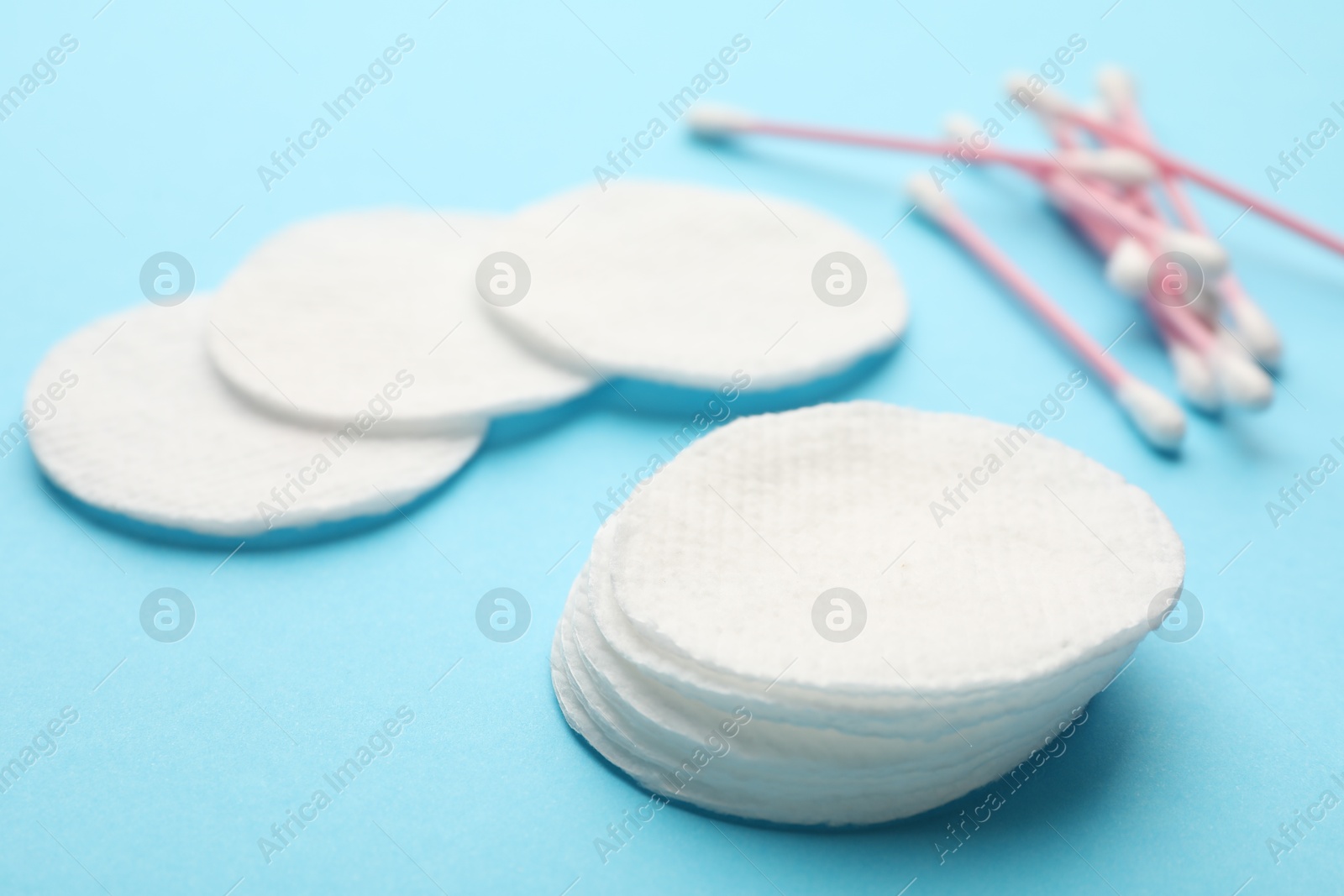 Photo of Cotton pads and swabs on light blue background, closeup