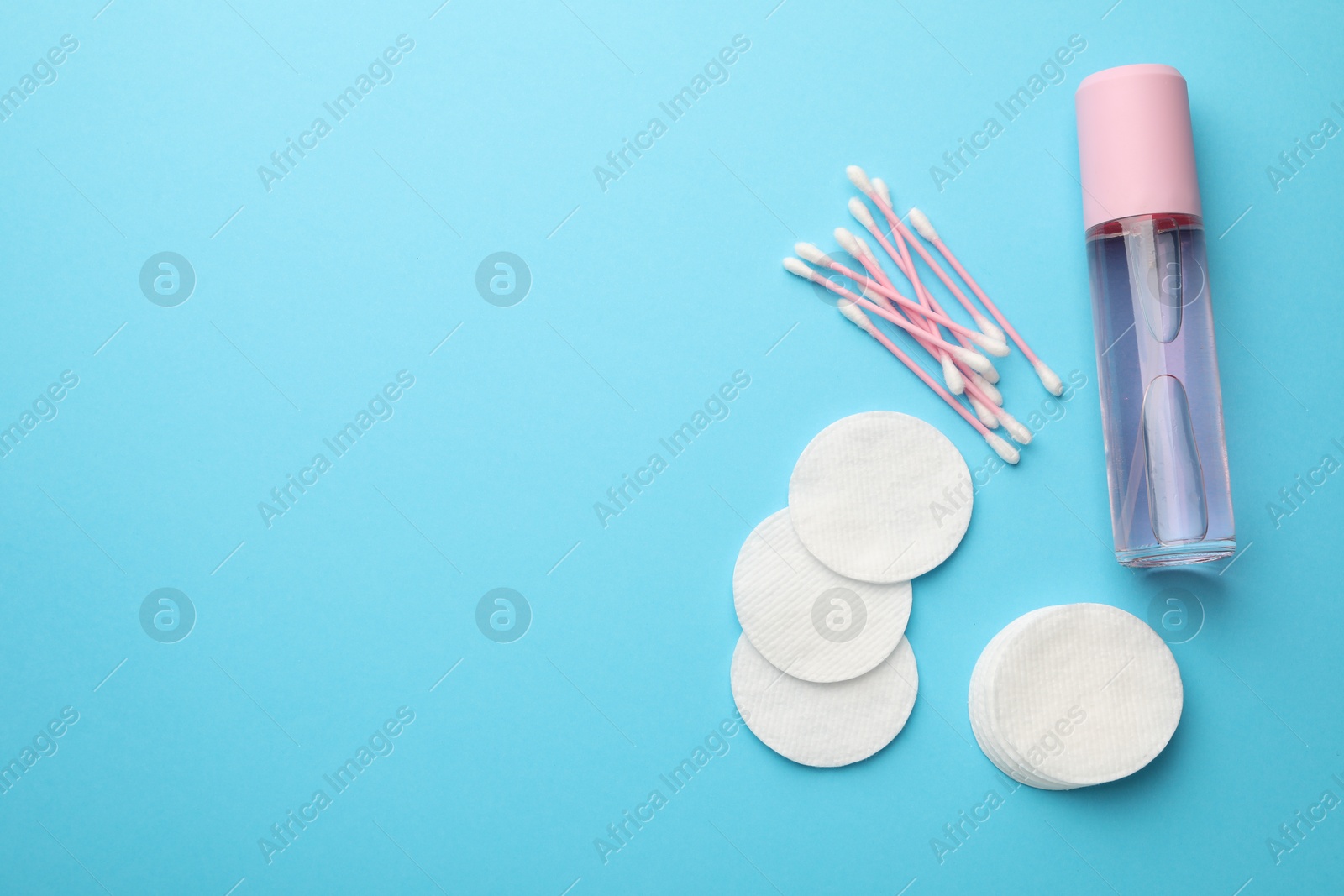 Photo of Cotton pads, bottle of cosmetic product and swabs on light blue background, flat lay. Space for text