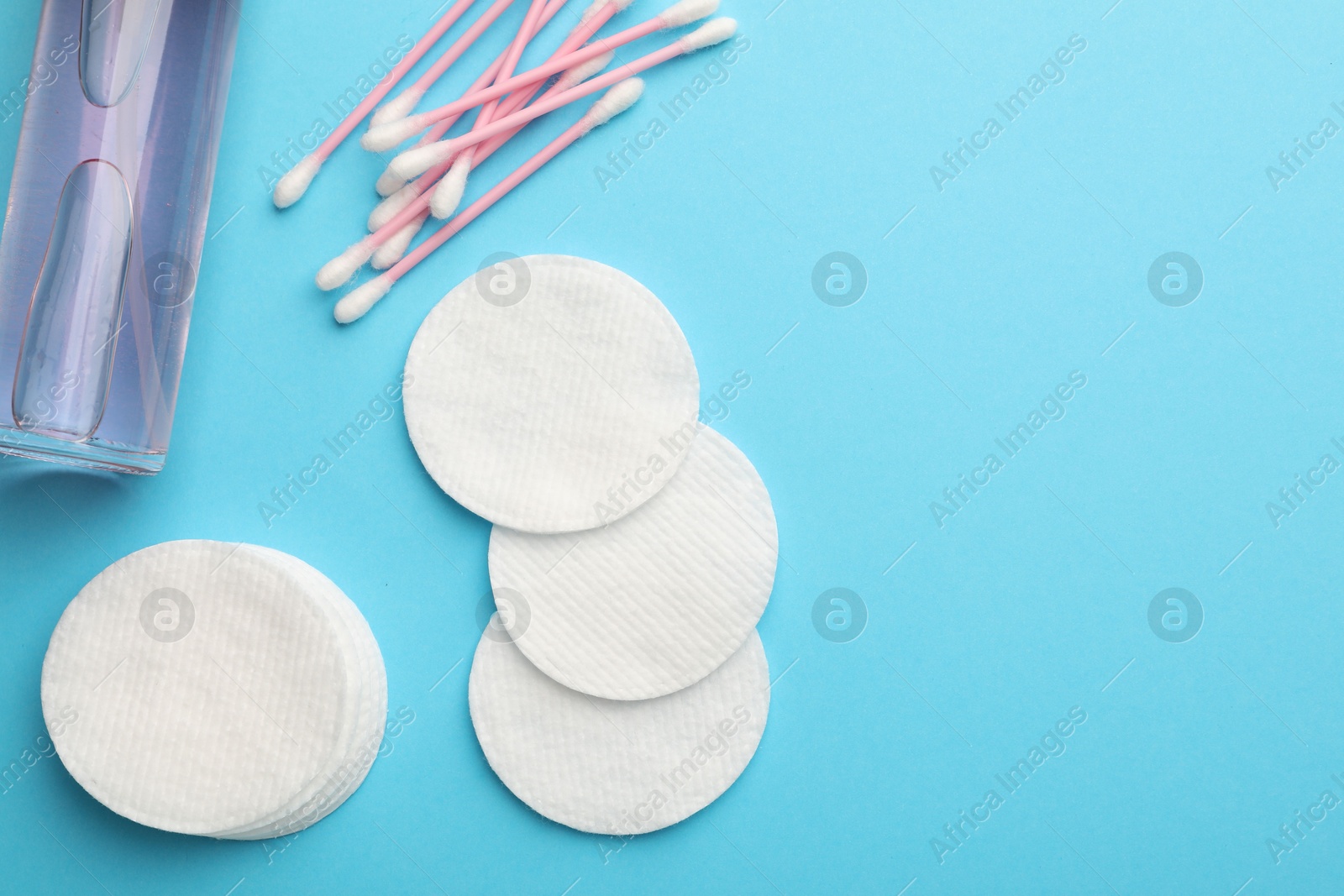 Photo of Cotton pads, bottle of cosmetic product and swabs on light blue background, flat lay. Space for text