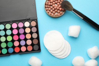 Photo of Cotton pads, balls, eyeshadow, blush and brush on light blue background, flat lay