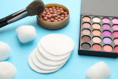 Photo of Cotton pads, balls, eyeshadow, blush and brush on light blue background, closeup