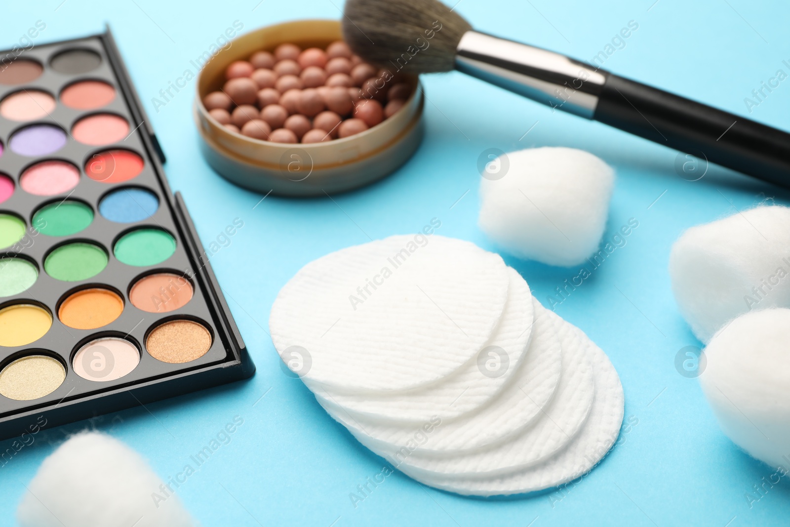 Photo of Cotton pads, balls, eyeshadow, blush and brush on light blue background, closeup