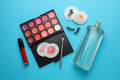 Photo of Dirty cotton pads, micellar water, false eyelashes and makeup products on light blue background, flat lay