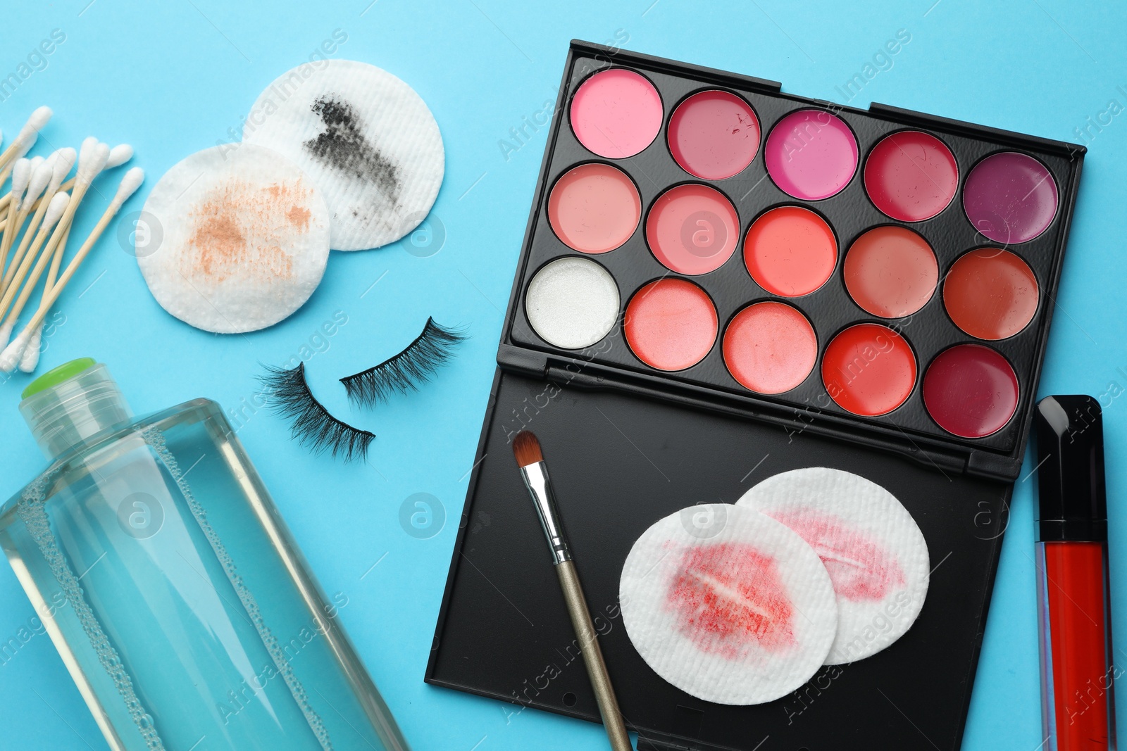 Photo of Dirty cotton pads, micellar water, swabs, false eyelashes and makeup products on light blue background, flat lay