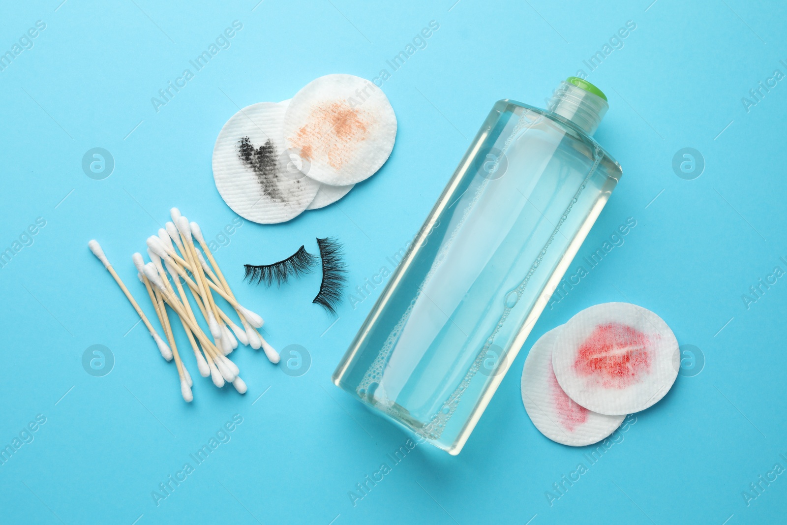 Photo of Dirty cotton pads, swabs, bottle of makeup remover and false eyelashes on light blue background, flat lay