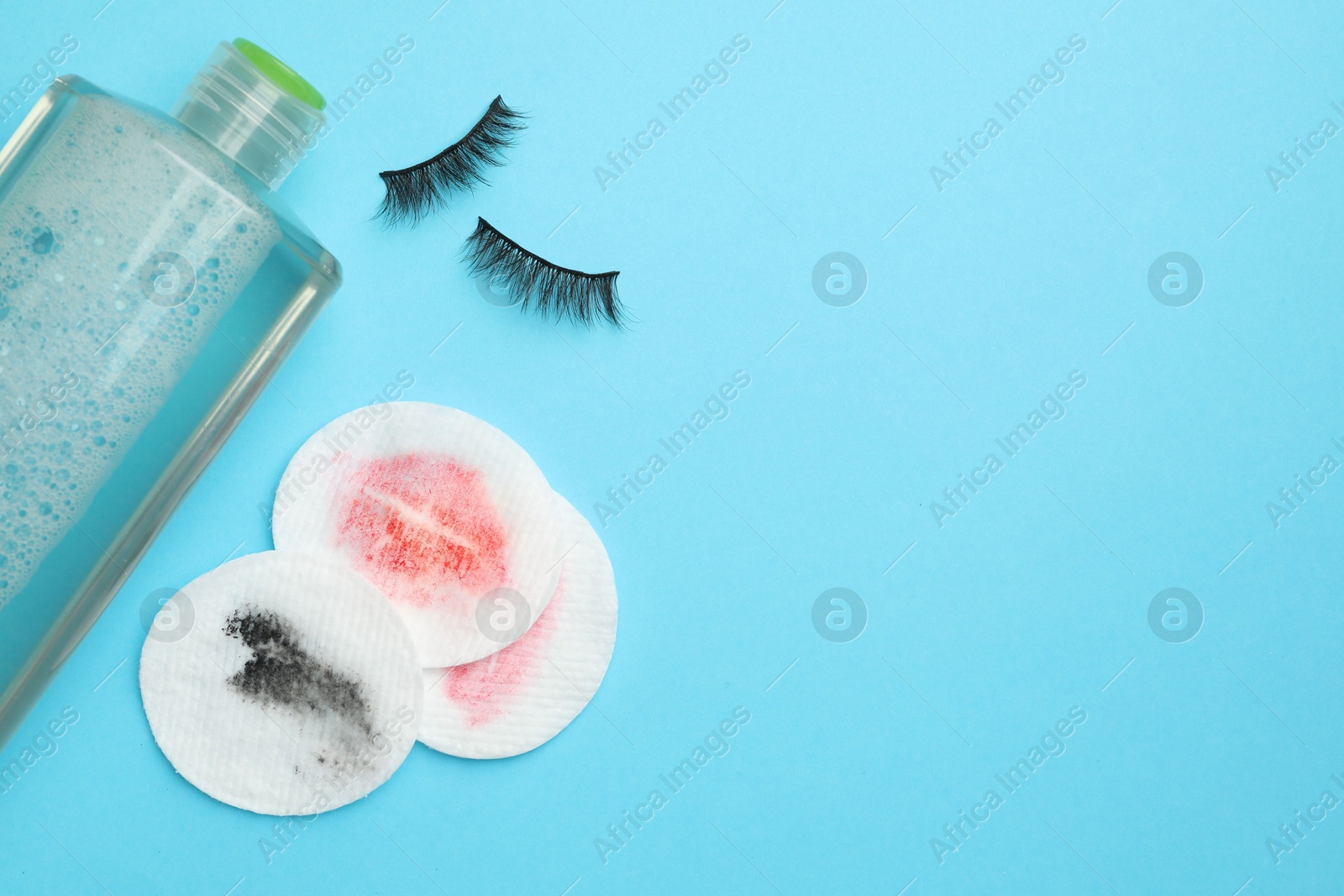 Photo of Dirty cotton pads, bottle of makeup remover and false eyelashes on light blue background, flat lay. Space for text