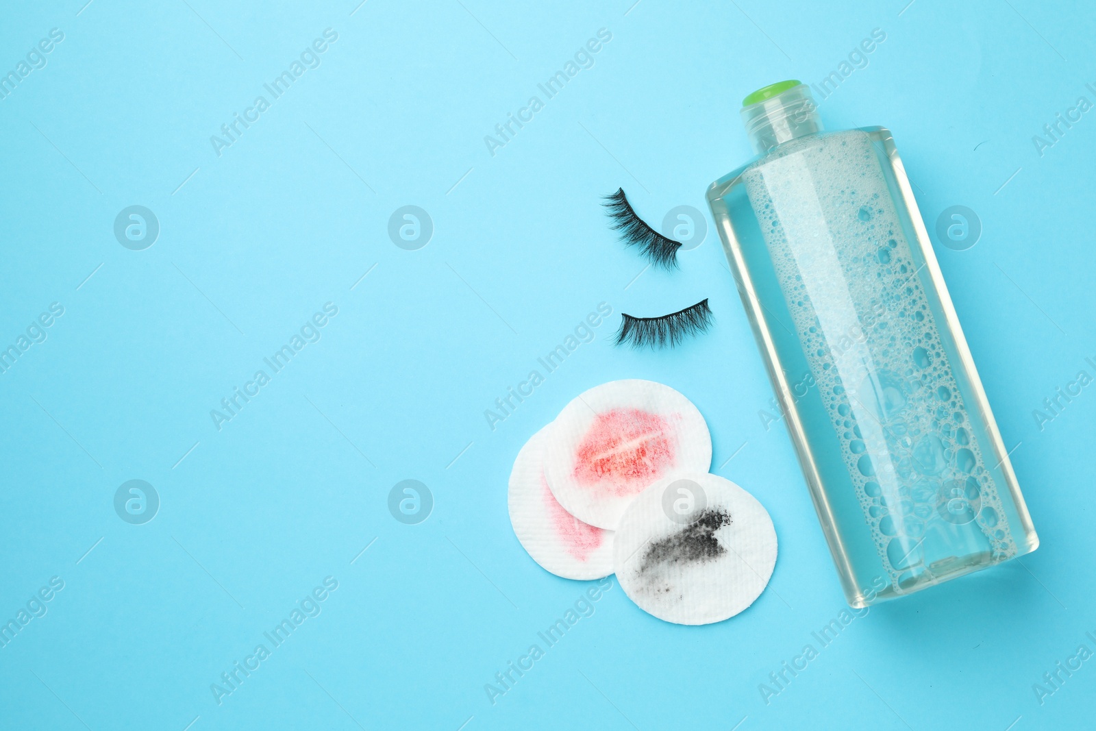 Photo of Dirty cotton pads, bottle of makeup remover and false eyelashes on light blue background, flat lay. Space for text