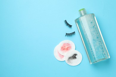 Photo of Dirty cotton pads, bottle of makeup remover and false eyelashes on light blue background, flat lay. Space for text