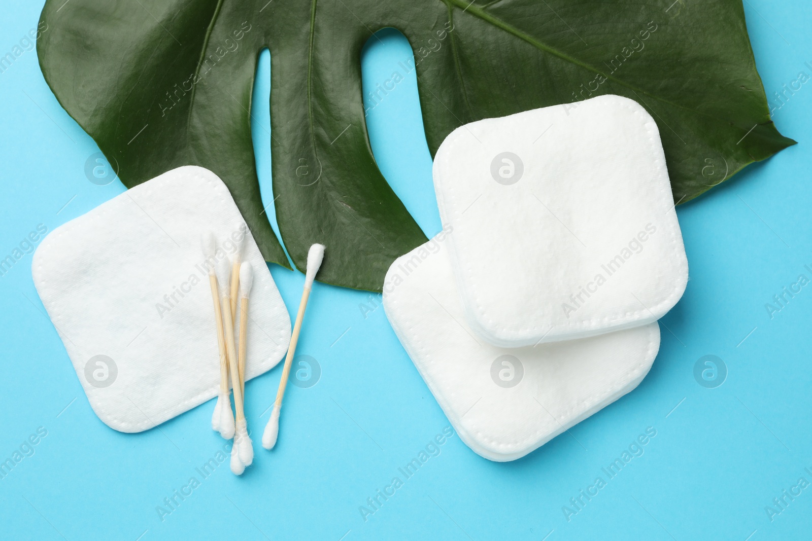 Photo of Cotton pads, swabs and monstera leaf on light blue background, flat lay