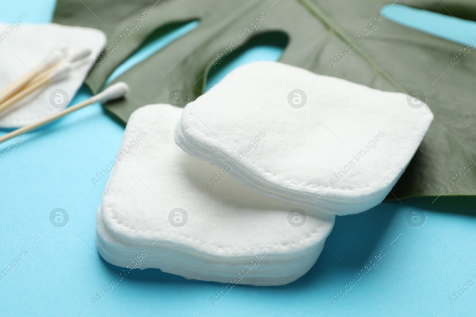 Photo of Cotton pads, swabs and monstera leaf on light blue background, closeup