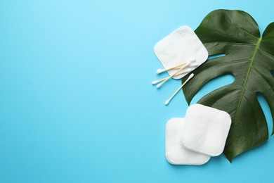 Photo of Cotton pads, swabs and monstera leaf on light blue background, flat lay. Space for text