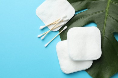 Photo of Cotton pads, swabs and monstera leaf on light blue background, flat lay. Space for text