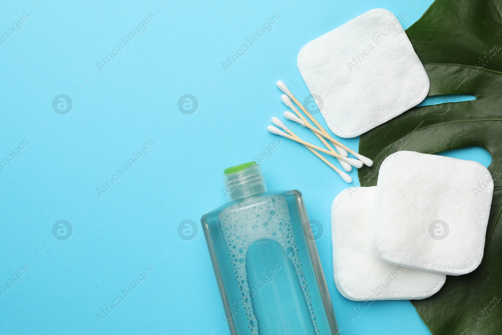 Photo of Cotton pads, swabs, cosmetic product and monstera leaf on light blue background, flat lay. Space for text