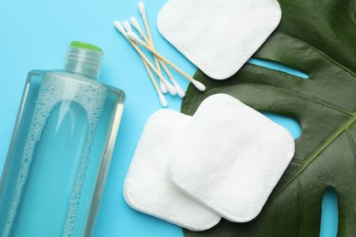 Photo of Cotton pads, swabs, cosmetic product and monstera leaf on light blue background, flat lay