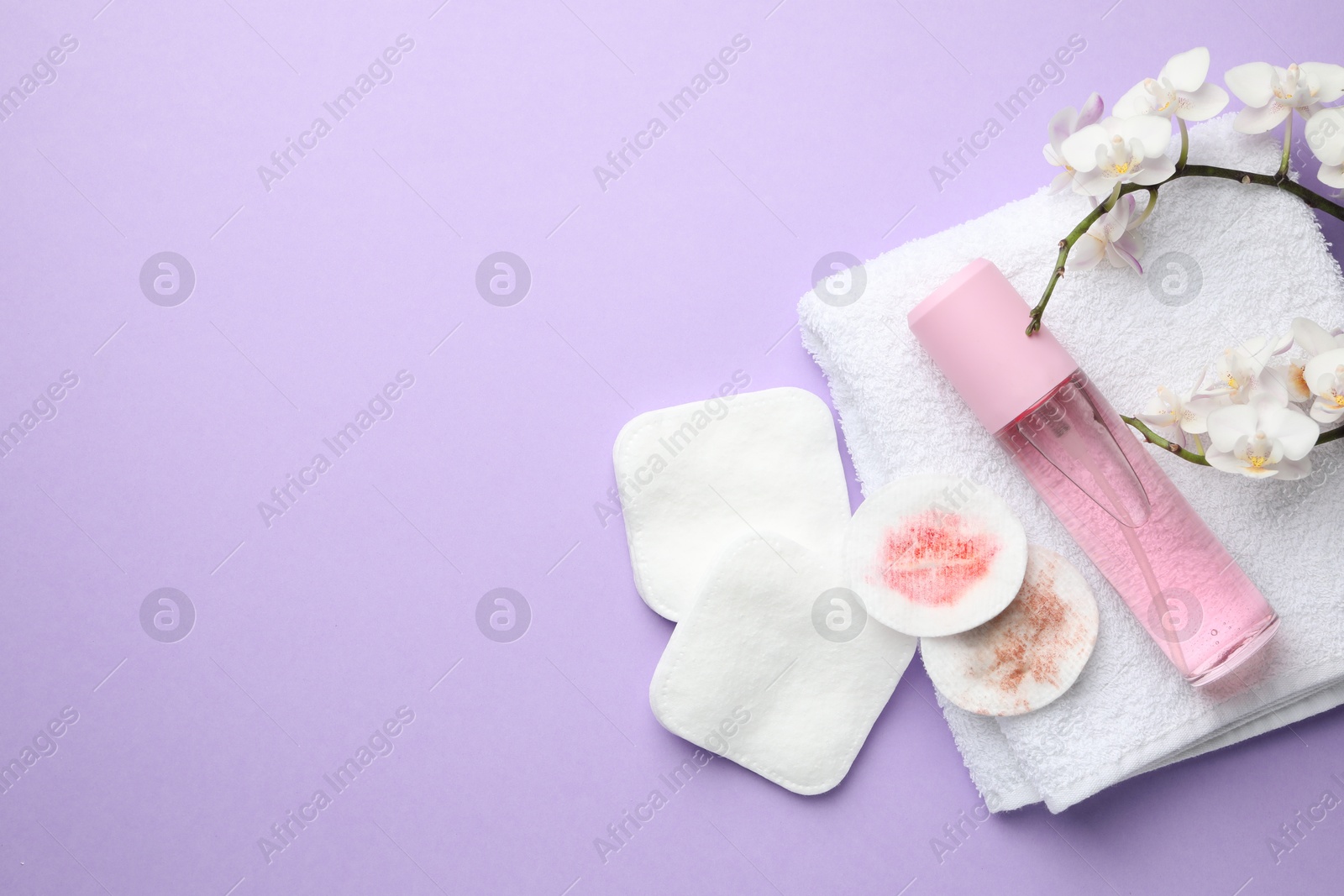 Photo of Dirty cotton pads, cosmetic product, towel and orchid branch on violet background, flat lay. Space for text