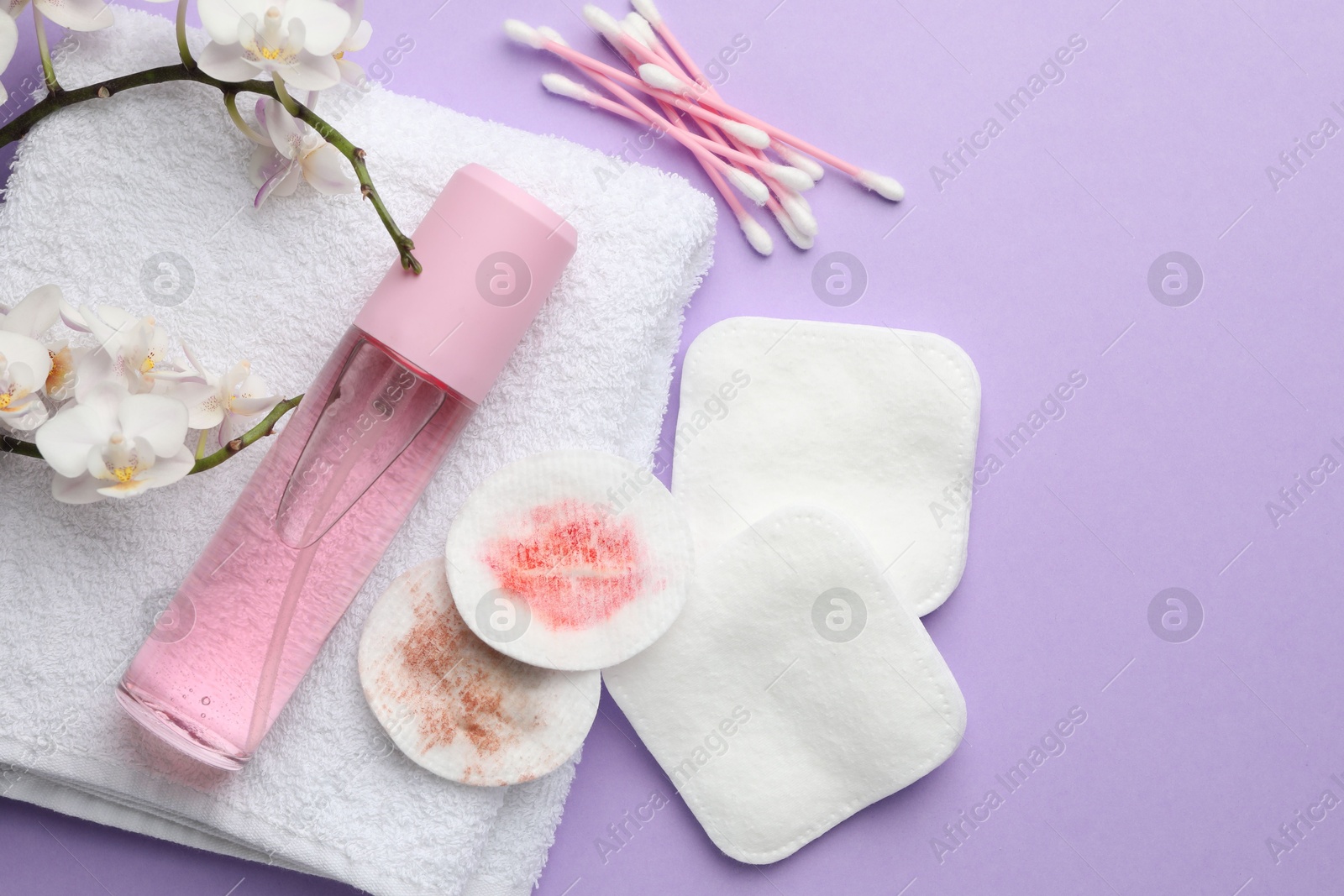 Photo of Dirty cotton pads, swabs, cosmetic product, towel and orchid branch on violet background, flat lay. Space for text