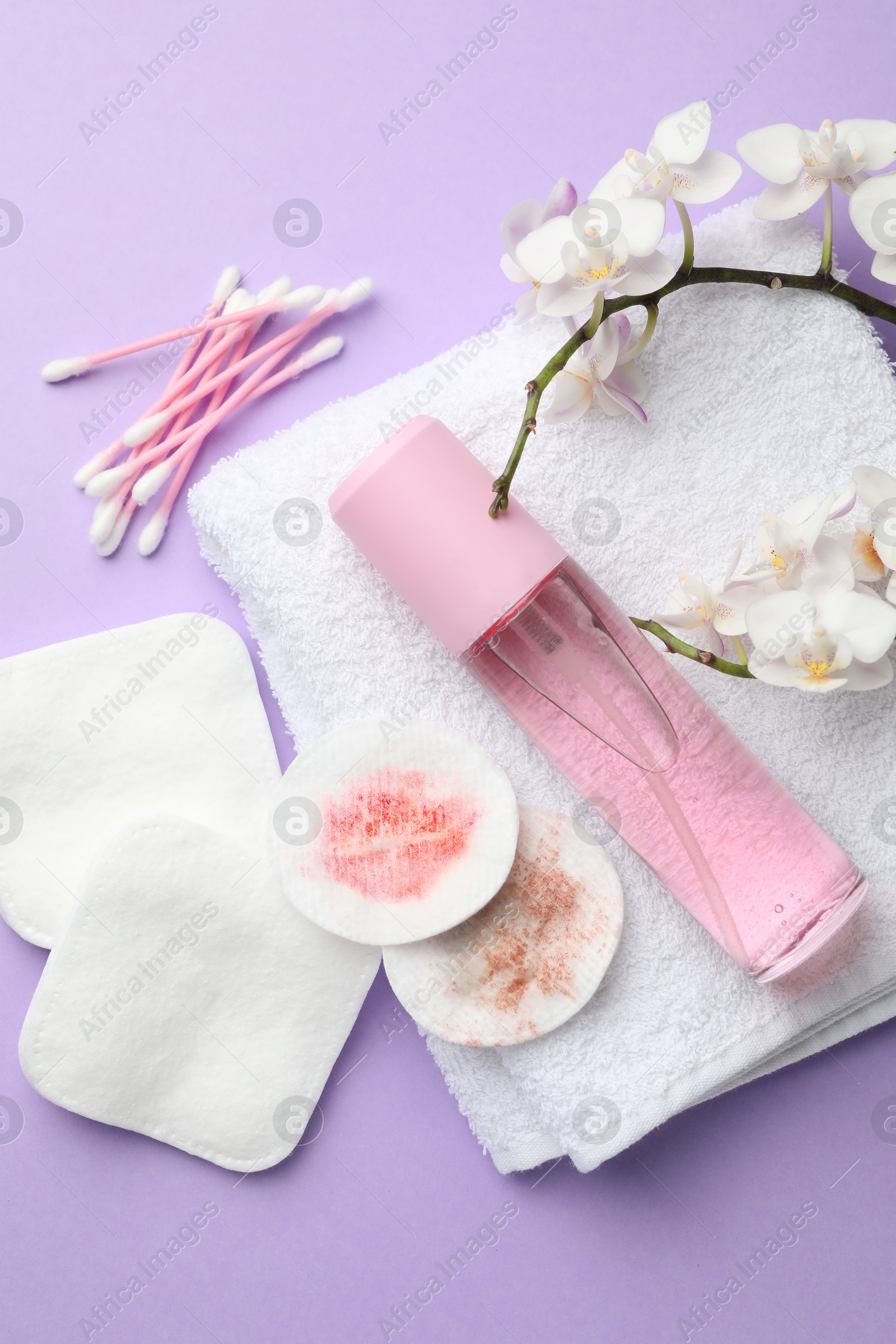 Photo of Dirty cotton pads, swabs, cosmetic product, towel and orchid branch on violet background, flat lay