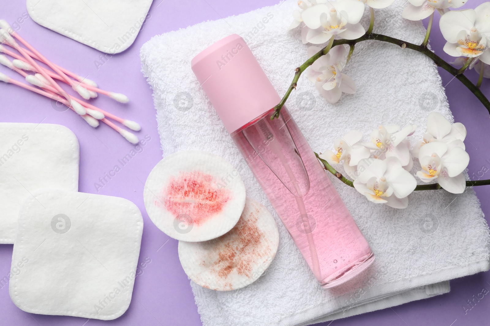 Photo of Dirty cotton pads, swabs, cosmetic product, towel and orchid branch on violet background, flat lay