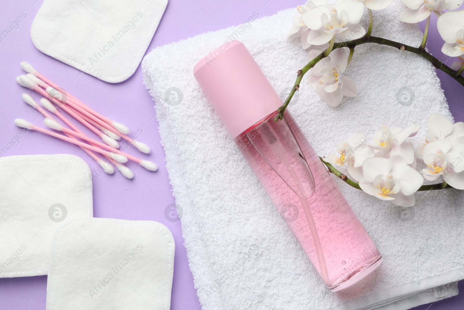 Photo of Cotton pads, swabs, cosmetic product, towel and orchid branch on violet background, flat lay