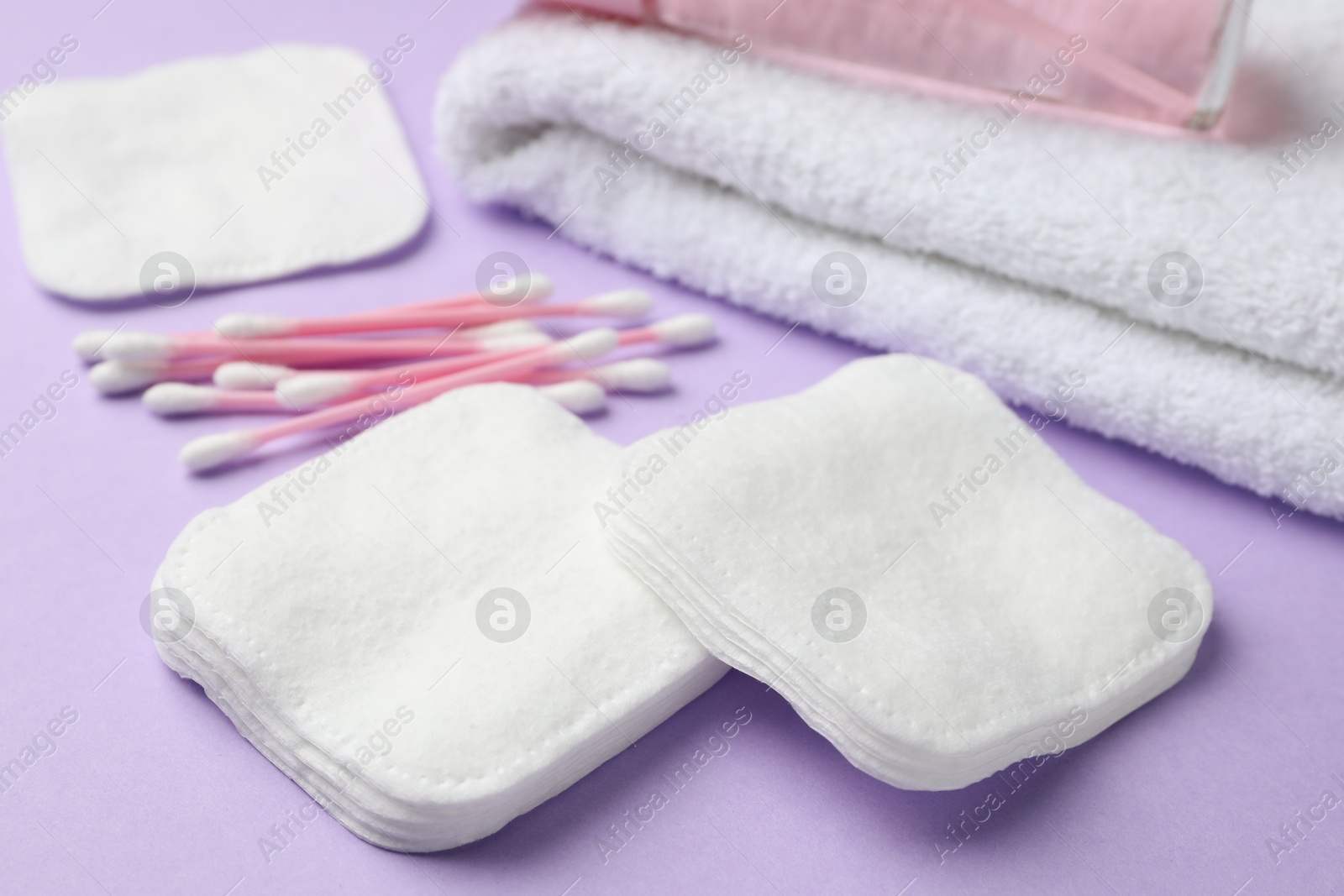 Photo of Cotton pads, swabs, towel and orchid branch on violet background, closeup