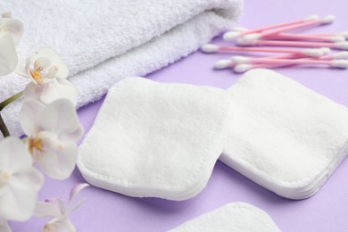 Photo of Cotton pads, swabs, towel and orchid branch on violet background, closeup