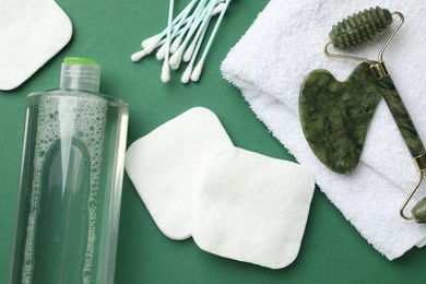 Photo of Cotton pads, swabs, cosmetic product, face roller, gua sha tool and towel on green background, flat lay