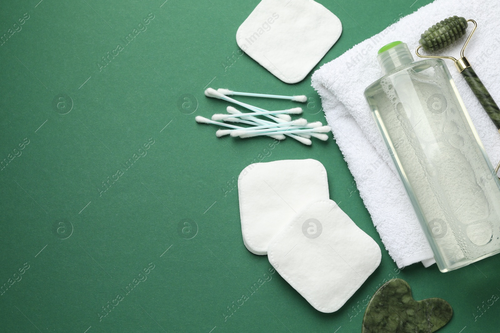 Photo of Cotton pads, swabs, cosmetic product, face roller, gua sha tool and towel on green background, flat lay. Space for text