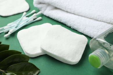 Photo of Cotton pads, swabs, cosmetic product, towel and leaves on green background, closeup