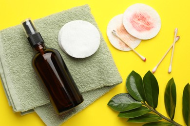 Photo of Dirty cotton pads, swabs, cosmetic product, towel and green branch on yellow background, flat lay