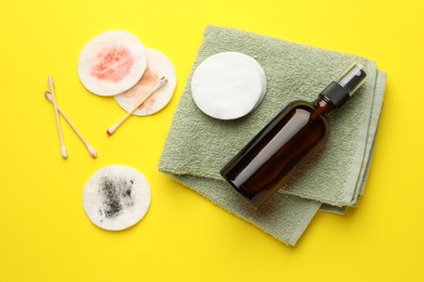 Photo of Dirty cotton pads, swabs, cosmetic product and towel on yellow background, flat lay