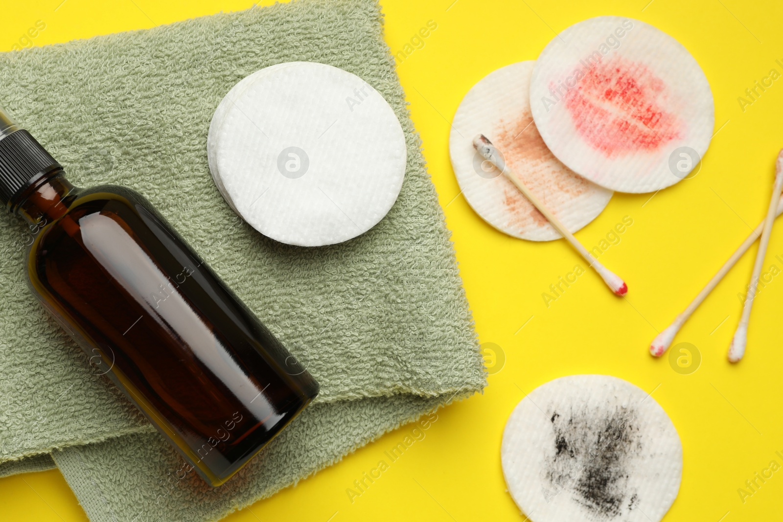 Photo of Dirty cotton pads, swabs, cosmetic product and towel on yellow background, flat lay