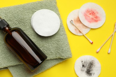 Photo of Dirty cotton pads, swabs, cosmetic product and towel on yellow background, flat lay