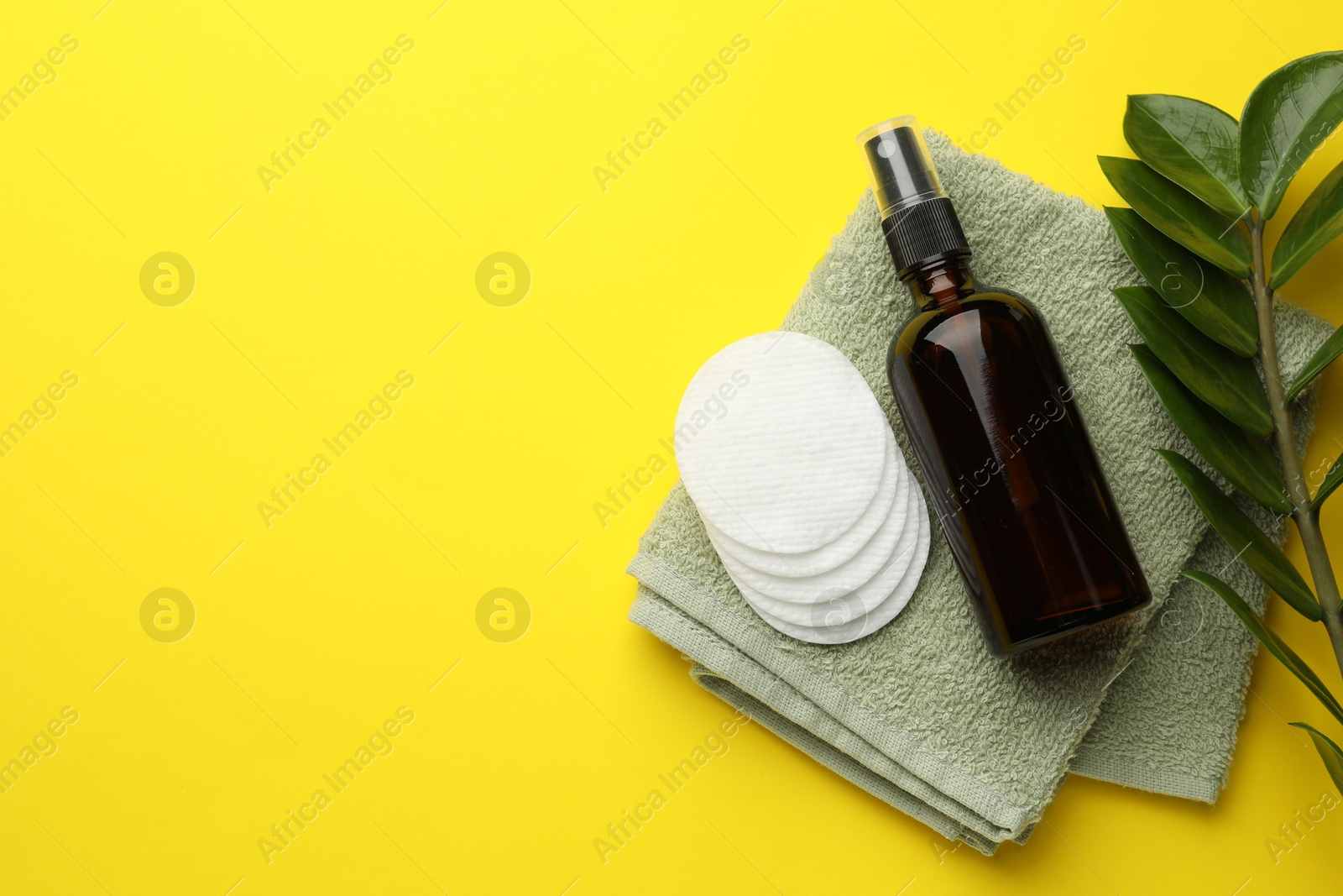 Photo of Cotton pads, cosmetic product, towel and green branch on yellow background, flat lay. Space for text