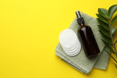 Photo of Cotton pads, cosmetic product, towel and green branch on yellow background, flat lay. Space for text