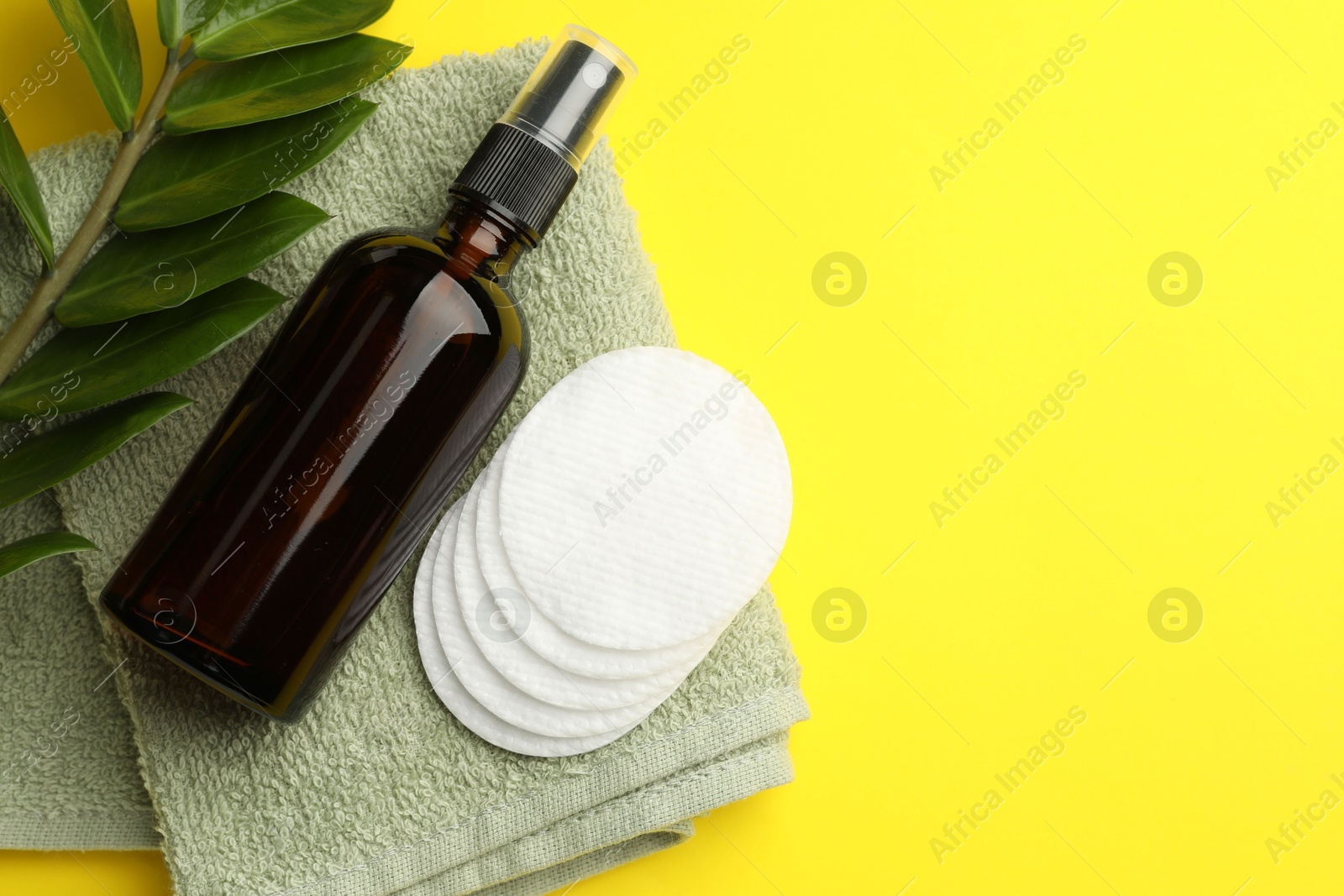 Photo of Cotton pads, cosmetic product, towel and green branch on yellow background, flat lay. Space for text