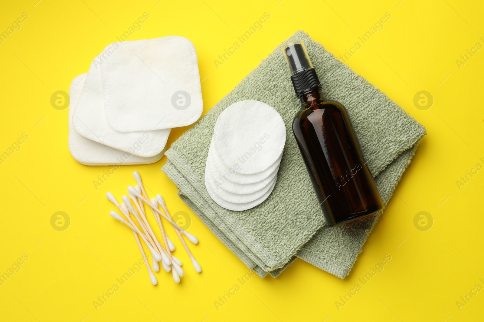 Photo of Cotton pads, cosmetic product, swabs and towel on yellow background, flat lay