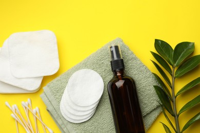 Photo of Cotton pads, cosmetic product, swabs, towel and green branch on yellow background, flat lay