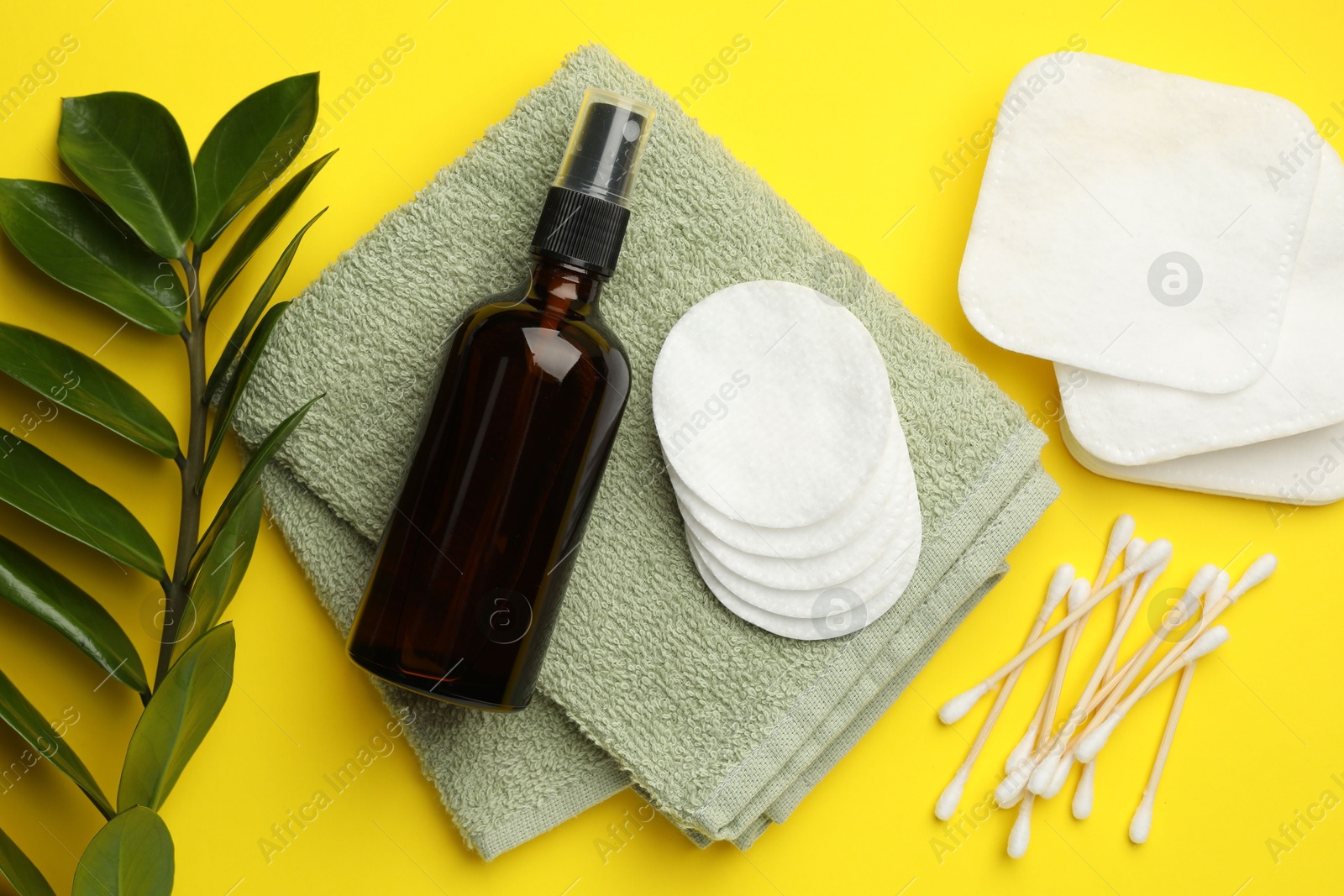 Photo of Cotton pads, cosmetic product, swabs, towel and green branch on yellow background, flat lay