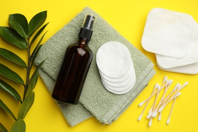 Photo of Cotton pads, cosmetic product, swabs, towel and green branch on yellow background, flat lay