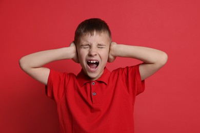 Photo of Little boy covering his ears on red background