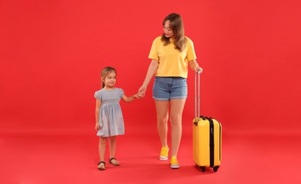 Photo of Traveller with suitcase. Young woman and cute little girl on red background