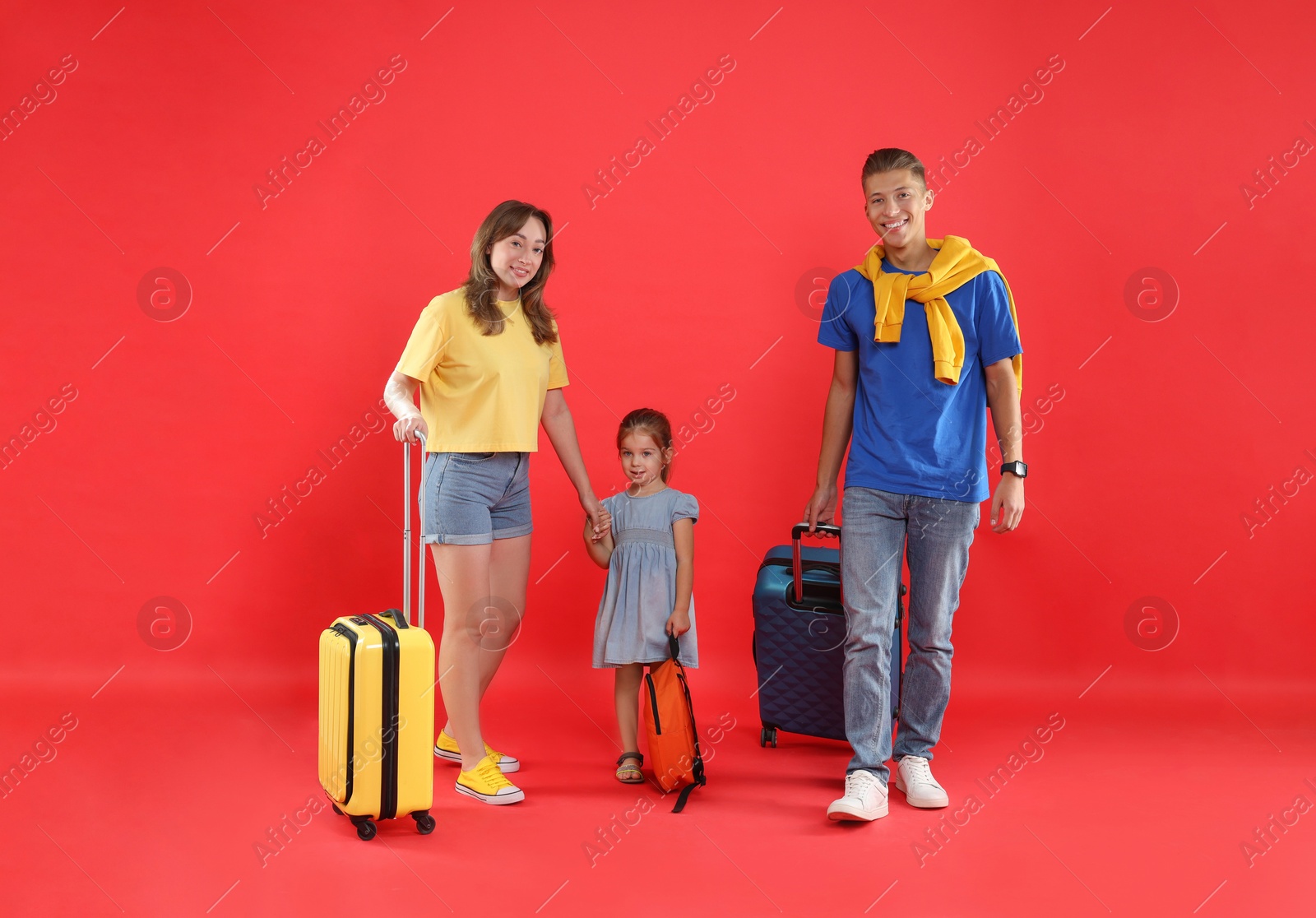 Photo of Travellers with suitcases and backpack. Happy family on red background