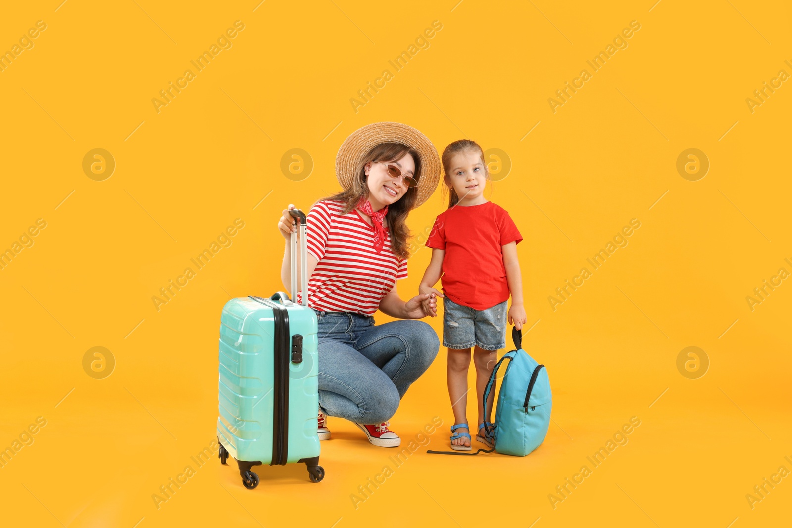 Photo of Travellers with suitcase and backpack. Young woman and cute little girl on yellow background