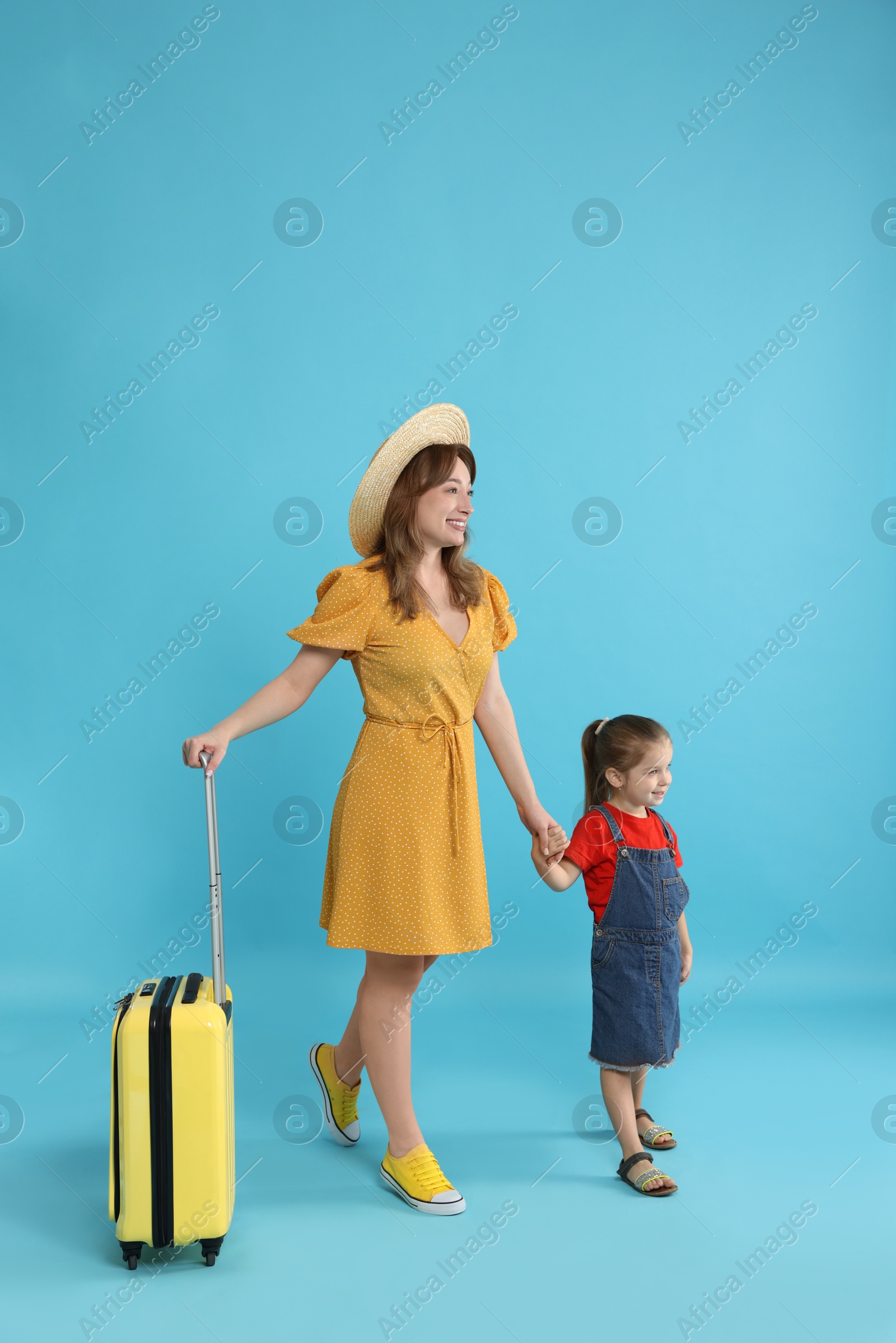 Photo of Traveller with suitcase. Young woman and cute little girl on light blue background