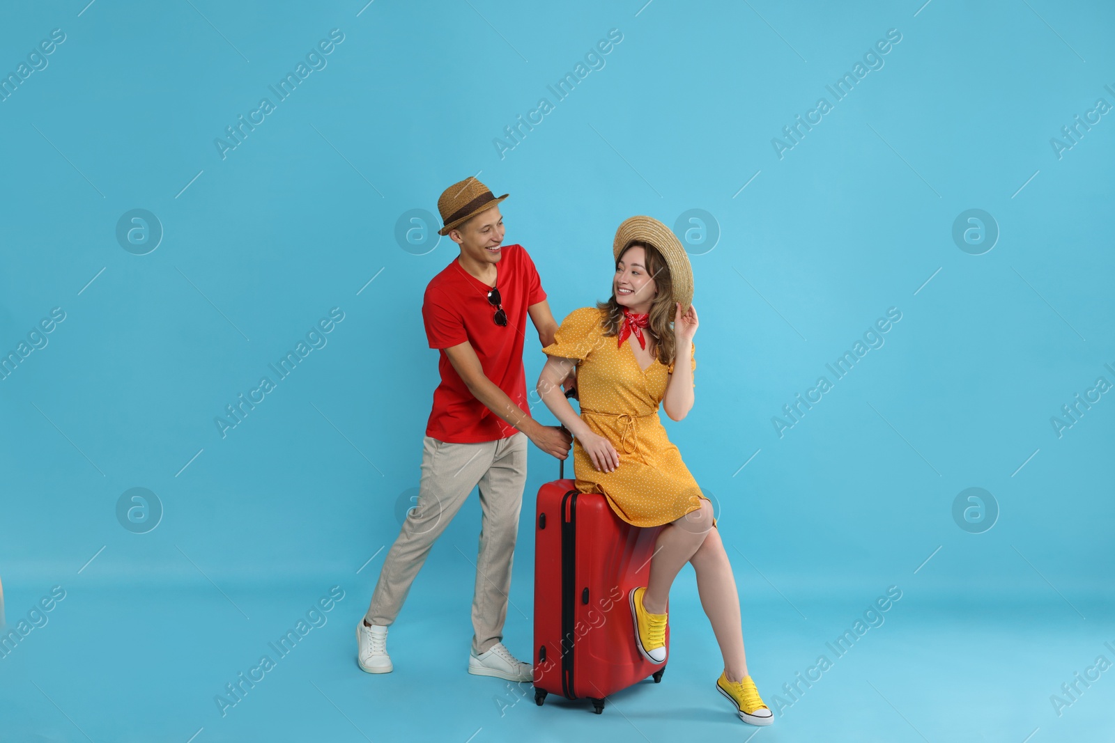 Photo of Happy travellers with suitcase on light blue background