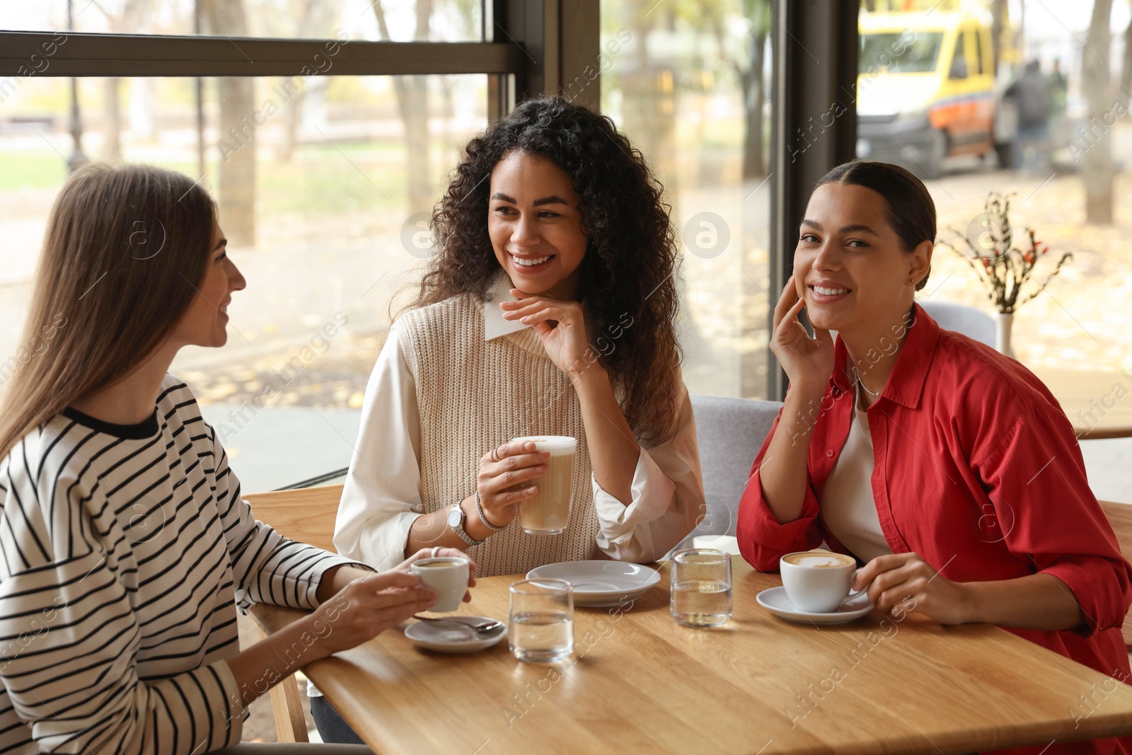 Photo of Happy women with coffee drinks chatting in cafe