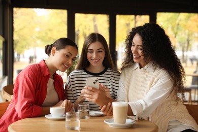 Photo of Women using smartphone while having coffee in cafe