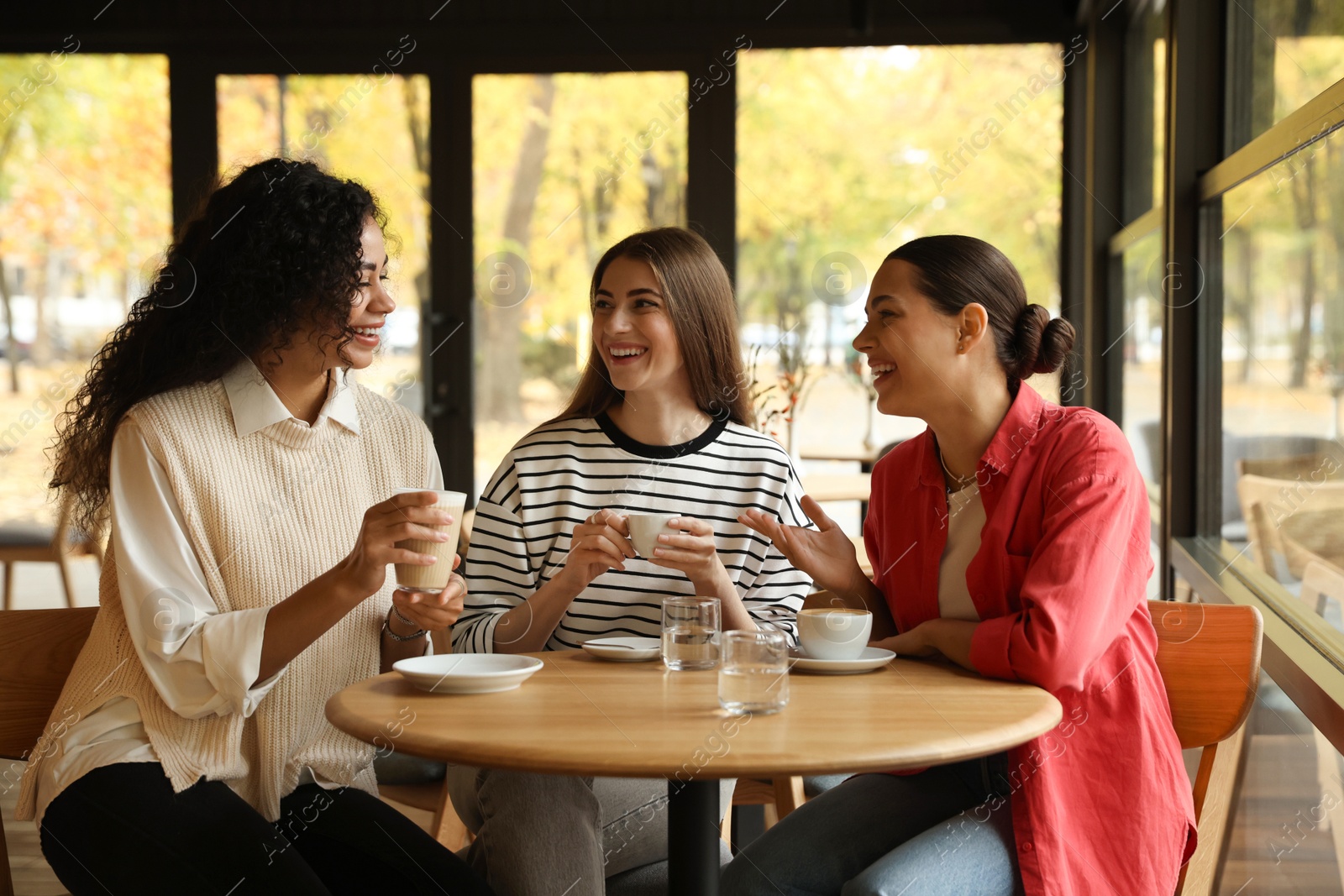 Photo of Happy women with coffee drinks chatting in cafe