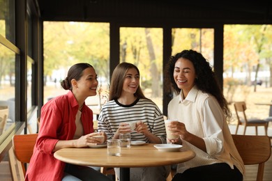 Photo of Happy women with coffee drinks chatting in cafe